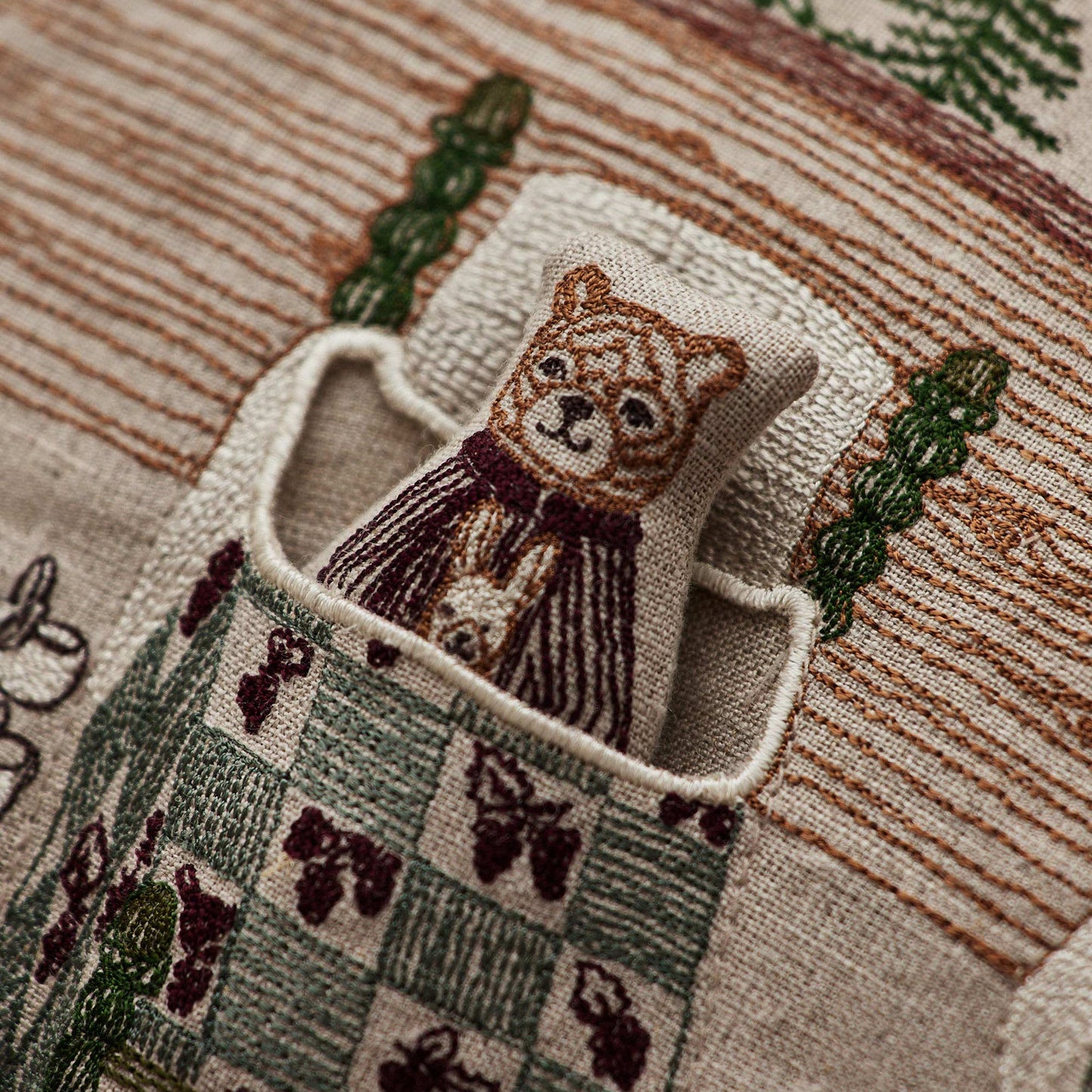 Coral and Tusk’s “Three Little Bears” embroidered linen pocket pillow featuring three bears tucked in bed with a puppy hiding in the doorway, measures 12” x 16”