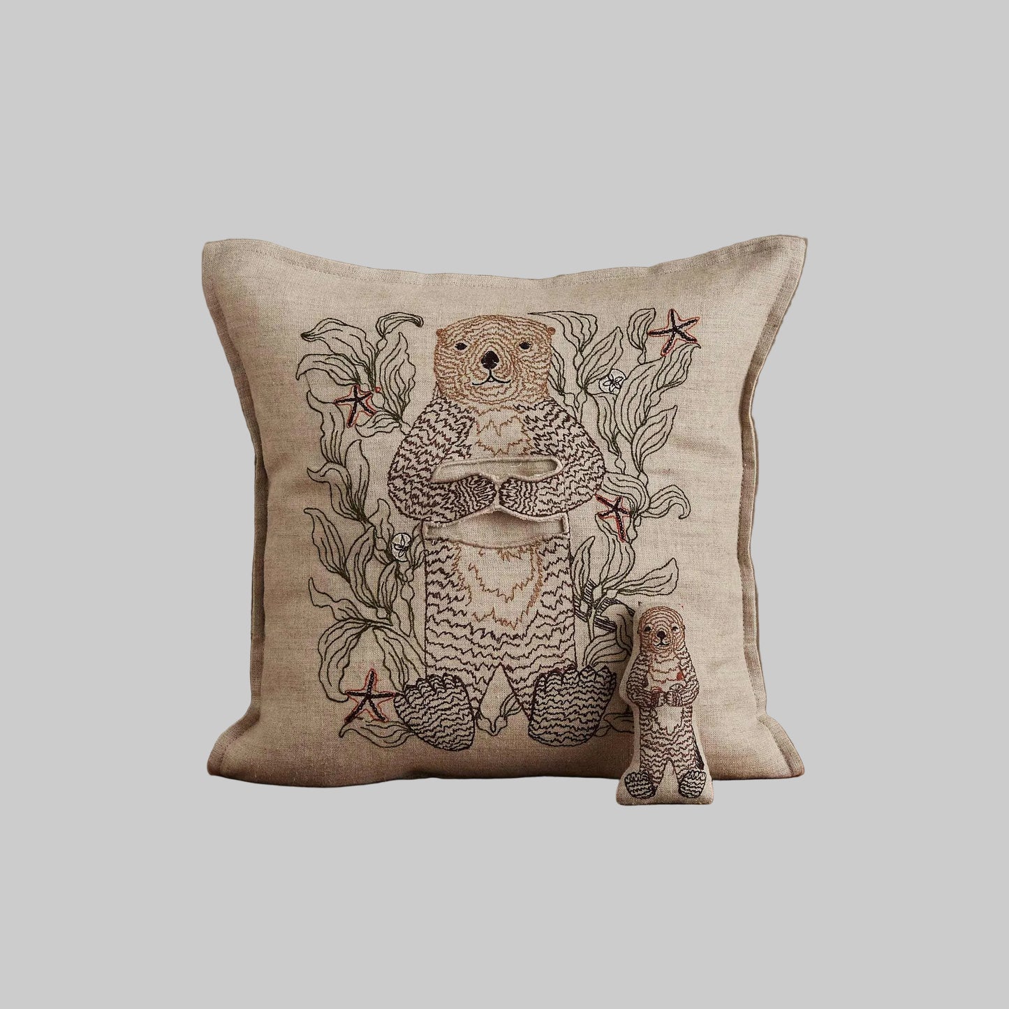 Coral and Tusk’s “Otter Mama” embroidered linen pocket pillow featuring a mother sea otter holding her pup in a sea of kelp