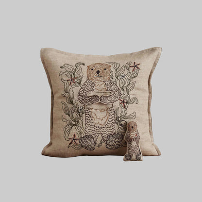 Coral and Tusk’s “Otter Mama” embroidered linen pocket pillow featuring a mother sea otter holding her pup in a sea of kelp