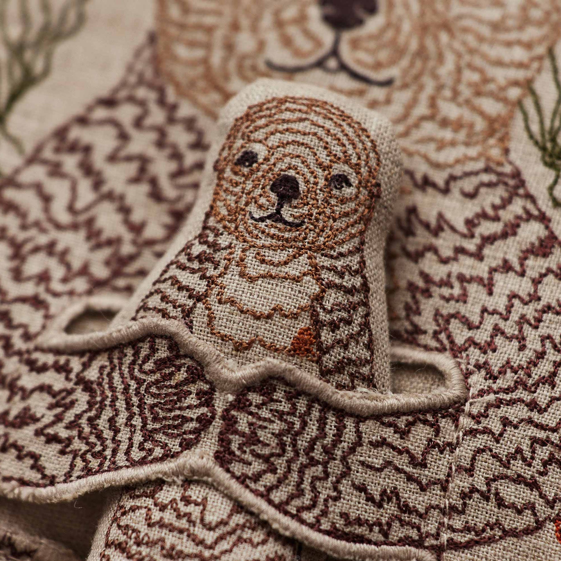 Coral and Tusk’s “Otter Mama” embroidered linen pocket pillow featuring a mother sea otter holding her pup in a sea of kelp