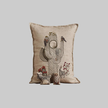 Coral and Tusk’s “Saguaro House” embroidered linen pocket pillow featuring desert animals sheltering in a cactus, measures 12” x 16”