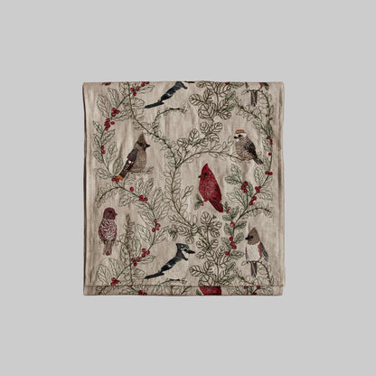 Coral and Tusk’s “Winter Birds” embroidered linen table runner featuring a variety of birds perching on branches of holly
