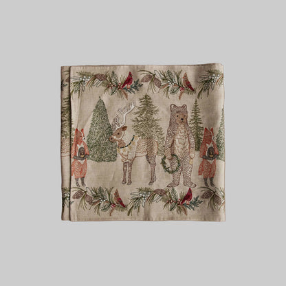 Coral and Tusk’s “Christmas Cheer” embroidered linen table runner featuring woodland animals holding wreaths surrounded by festive greenery