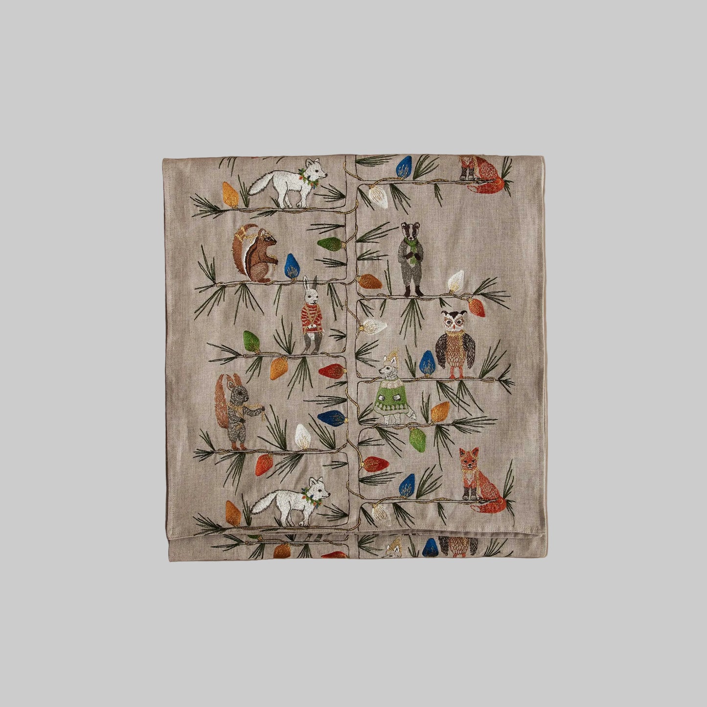 Coral and Tusk’s “Christmas Tree Trimmers” embroidered linen table runner featuring a group of festive animals decorating a Christmas tree