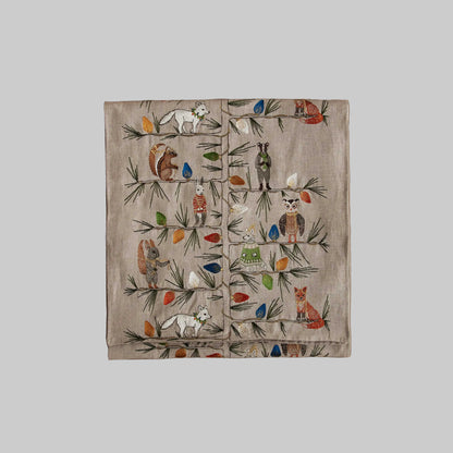 Coral and Tusk’s “Christmas Tree Trimmers” embroidered linen table runner featuring a group of festive animals decorating a Christmas tree