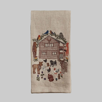 Coral and Tusk’s “Cabin Life” embroidered linen tea towel featuring a woodsy cabin surrounded by woodland creatures