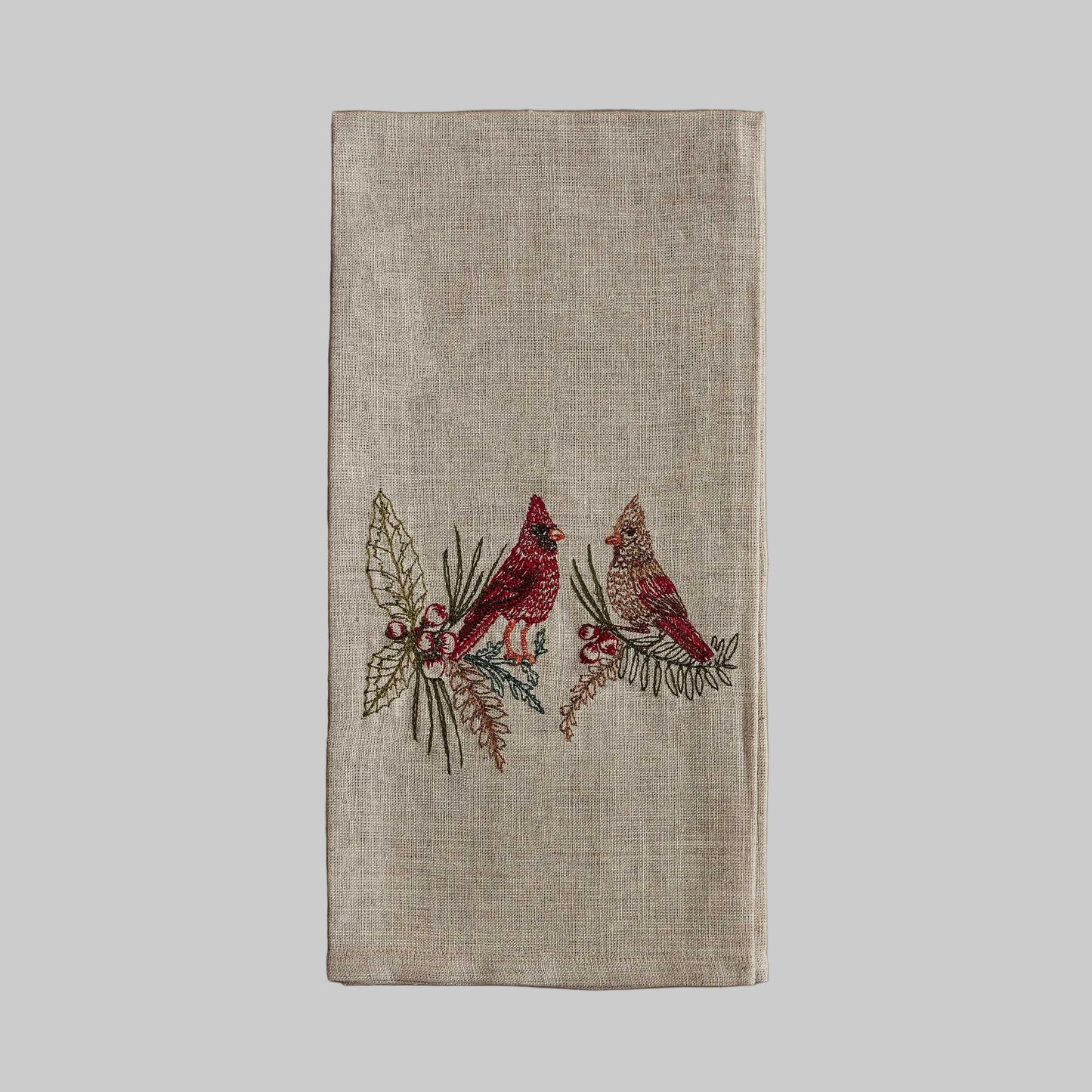 Coral and Tusk’s “Christmas Cardinals” embroidered linen tea towel featuring a male and female cardinal sitting on branches of holly and pine