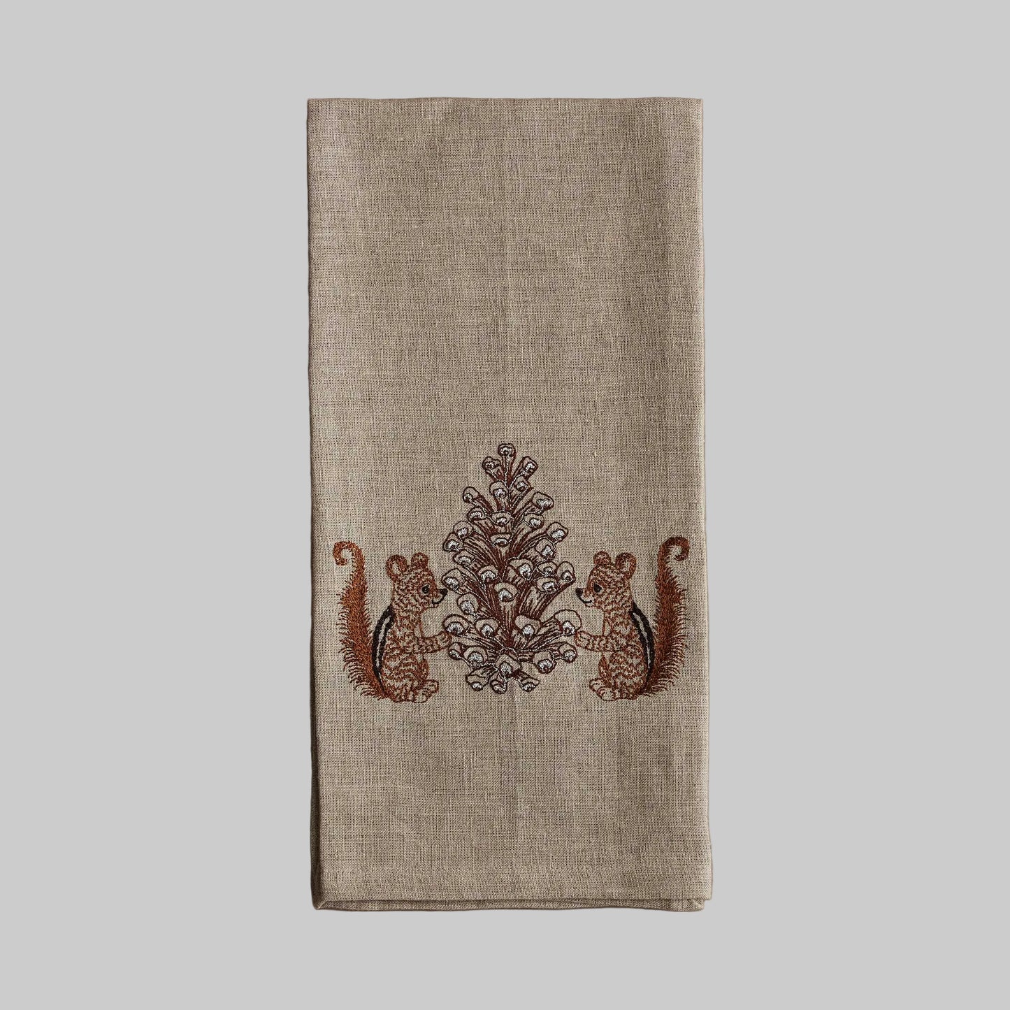 Coral and Tusk’s “Chipmunks with Pinecone” embroidered linen tea towel featuring two chipmunks holding a pinecone together