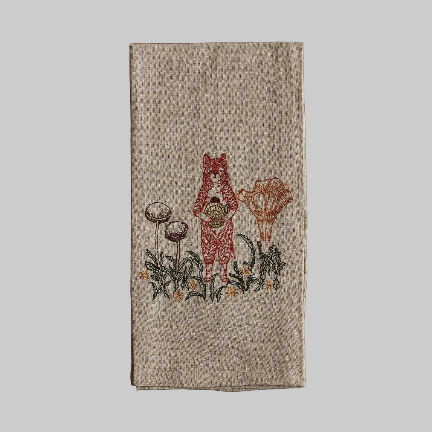 Coral and Tusk’s “Fox with Mushrooms” embroidered linen tea towel featuring a fox standing among several mushrooms