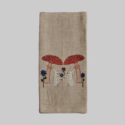 Coral and Tusk’s “Mushroom Bunny Friends” embroidered linen tea towel featuring two bunnies exchanging flowers under large mushrooms