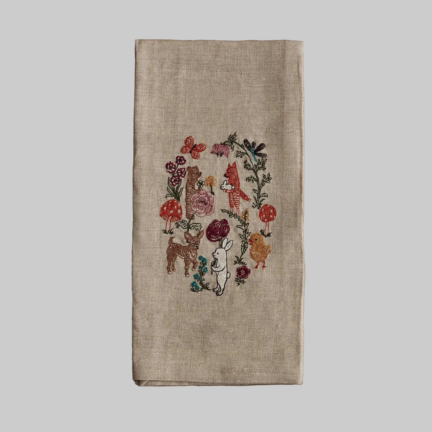 Coral and Tusk’s “Secret Garden” embroidered linen tea towel featuring a variety of animal friends gathering in a garden