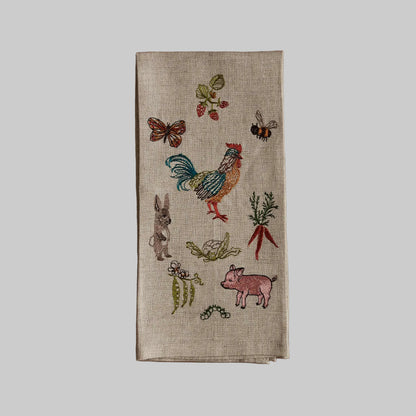 Coral and Tusk’s “Garden Gathering” embroidered linen tea towel featuring a group of farm animals, pollinators, and produce