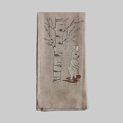 Coral and Tusk’s “Snowshoe Hare” embroidered linen tea towel featuring a white hair snowshoeing past an aspen tree