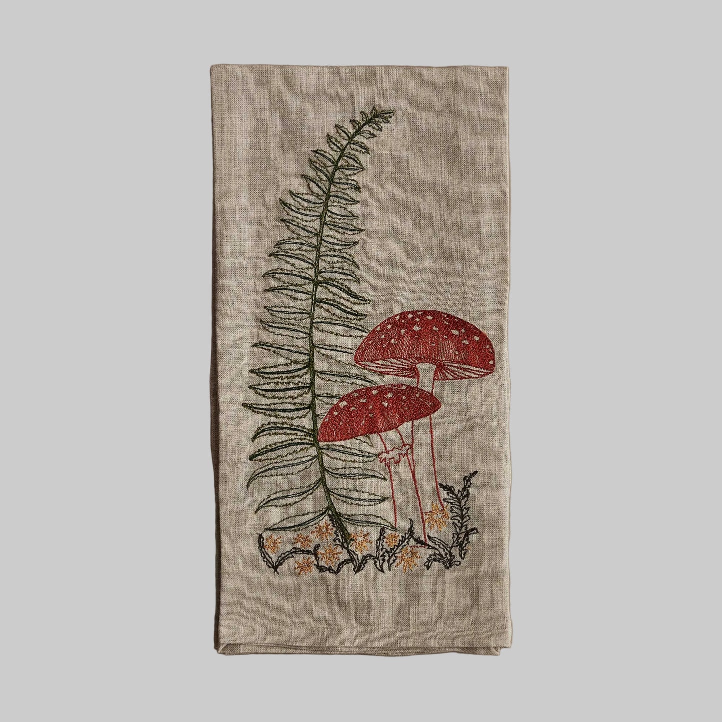 Coral and Tusk’s “Lady Fern” embroidered linen tea towel featuring two mushrooms next to a fern frond 