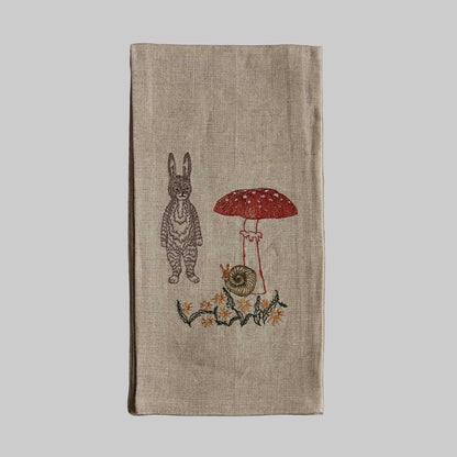 Coral and Tusk’s “Bunny with Mushrooms” embroidered linen tea towel featuring a gray bunny standing next to a tall mushroom