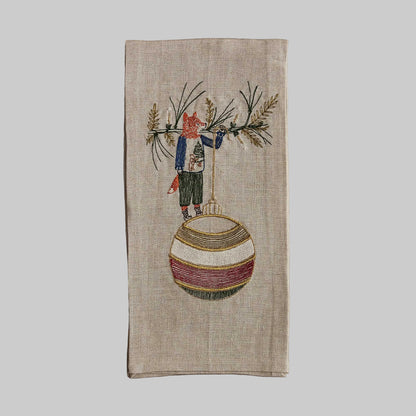 Coral and Tusk’s “Deck the Halls Fox” embroidered linen tea towel featuring a fox standing on a large Christmas ornament