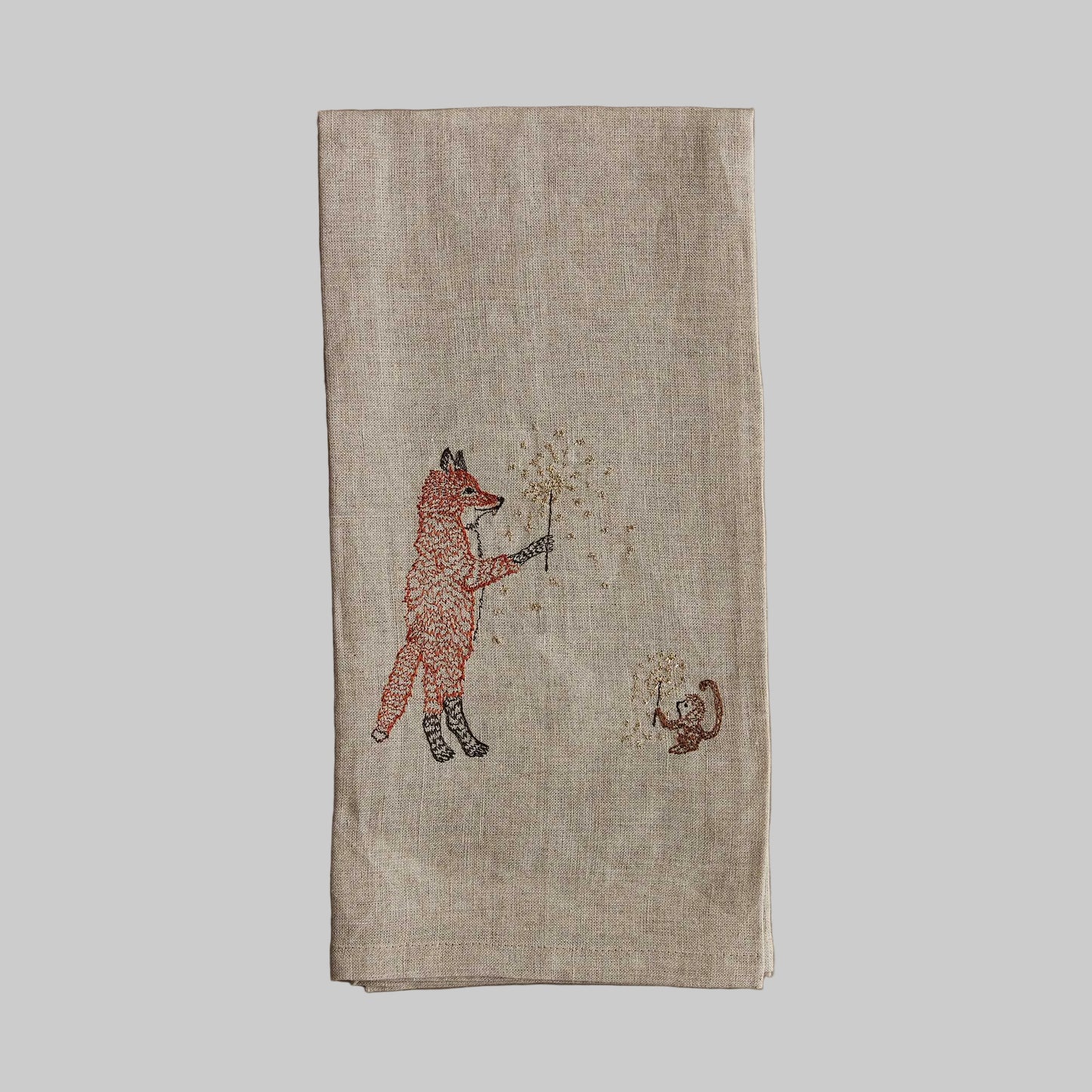 Coral and Tusk’s “Sparklers” embroidered linen tea towel featuring a fox and monkey holding sparklers