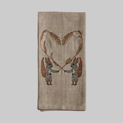 Coral and Tusk’s “Squirrels with Wheat” embroidered linen tea towel featuring two squirrels holding strands of wheat in the shape of a hearts