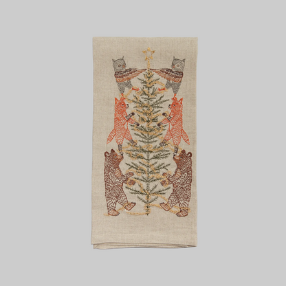 Coral and Tusk's "Tinsel Tree" embroidered linen tea towel featuring woodland animals decorating a Christmas tree with tinsel