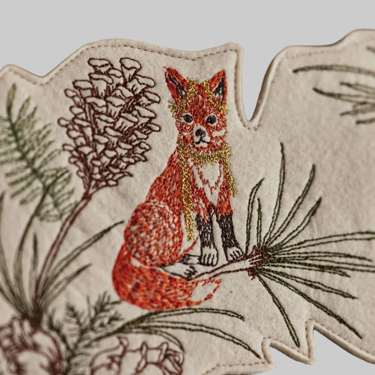 Coral and Tusk's "Tree Trimmers" embroidered holiday wreath featuring intricate pine needle designs and animal friends