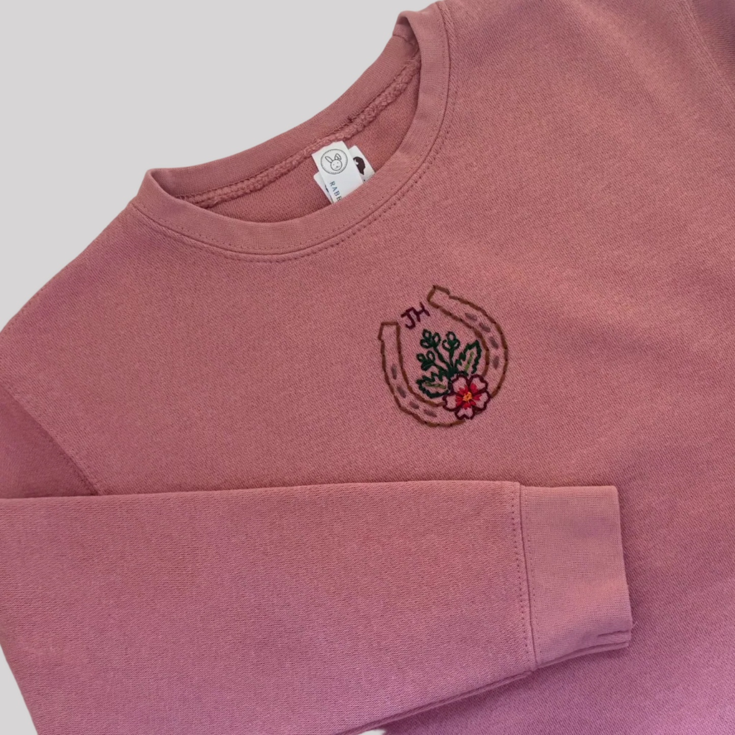 Roam Wild Good’s hand-embroidered kids sweatshirt in mauve featuring a horseshoe and floral design inspired by Jackson Hole, Wyoming