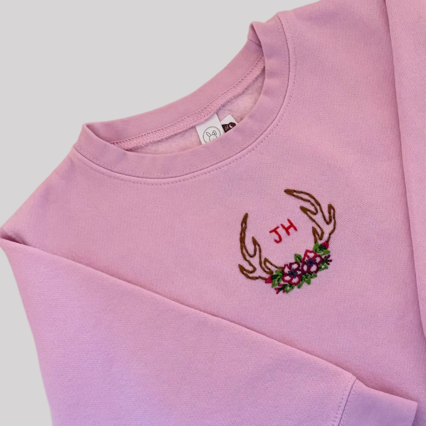 Roam Wild Good’s hand-embroidered kids sweatshirt in pink with an antler and floral design inspired by Jackson Hole, Wyoming