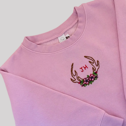 Roam Wild Good’s hand-embroidered kids sweatshirt in pink with an antler and floral design inspired by Jackson Hole, Wyoming