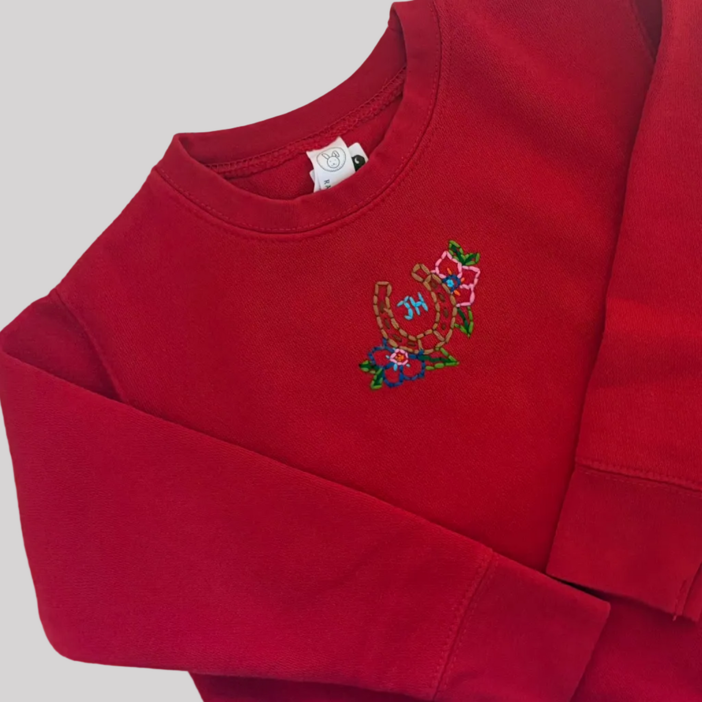 Roam Wild Good’s hand-embroidered kids sweatshirt In red with horseshoes and floral design inspired by Jackson Hole, Wyoming