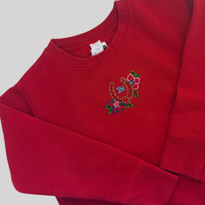 Roam Wild Good’s hand-embroidered kids sweatshirt In red with horseshoes and floral design inspired by Jackson Hole, Wyoming