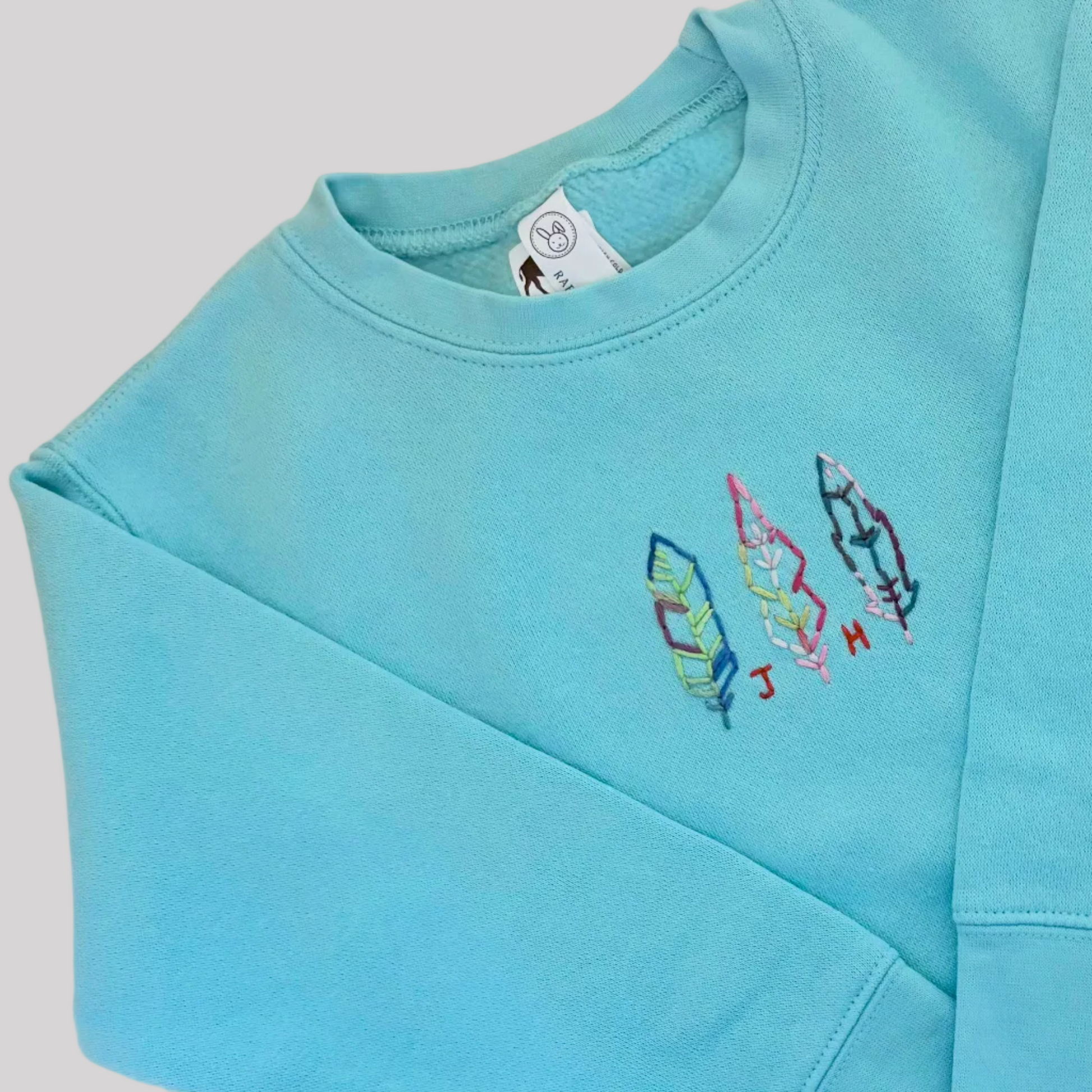 Roam Wild Good’s hand-embroidered kids sweatshirt in teal featuring a feather design inspired by Jackson Hole, Wyoming